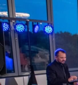 Chicago DJ performing at an event with blue stage lighting and glass windows in the background.