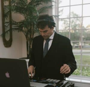 Chicago DJ in formal suit mixing music with headphones at a daytime event.