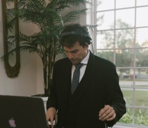 Chicago DJ in formal suit mixing music with headphones at a daytime event.
