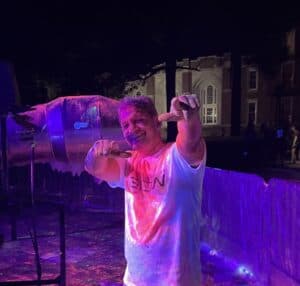 Man celebrating at an outdoor event with colorful lights and ice sculpture.
